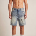 The Faded Denim Short in Blue, front on-body view showing the washed denim, distressed finish, and Volée crest graphic.