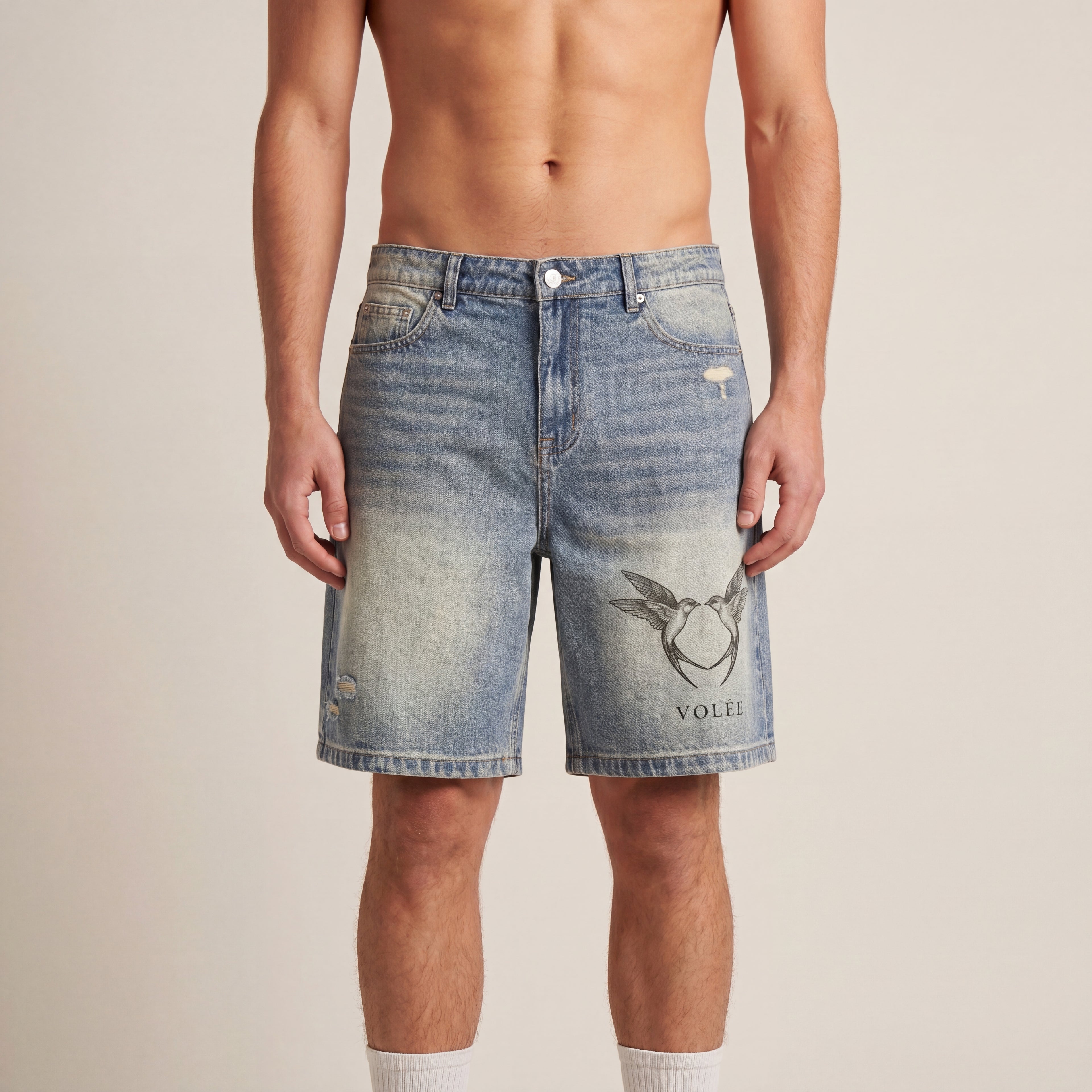 The Faded Denim Short in Blue, front on-body view showing the washed denim, distressed finish, and Volée crest graphic.