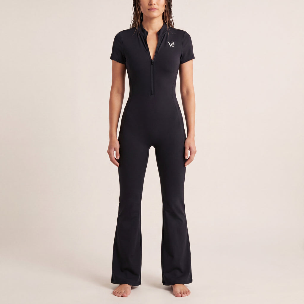 The Studio Jumpsuit in Black, front on-body view showing the quarter-zip neckline, white Vé chest mark, fitted torso, and flared leg.