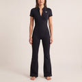 The Studio Jumpsuit in Black, front on-body view showing the quarter-zip neckline, white Vé chest mark, fitted torso, and flared leg.